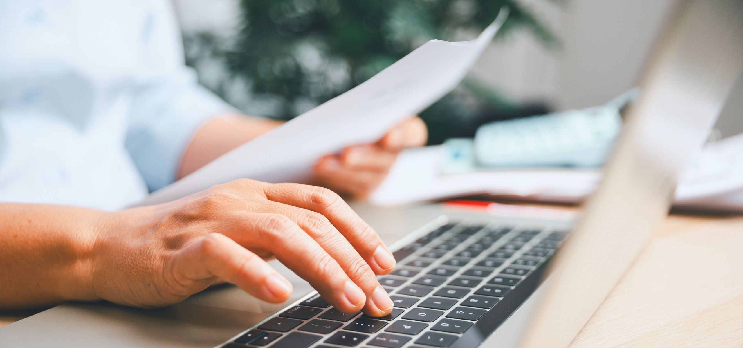 Close-up of hands reviewing a printed resume beside a laptop